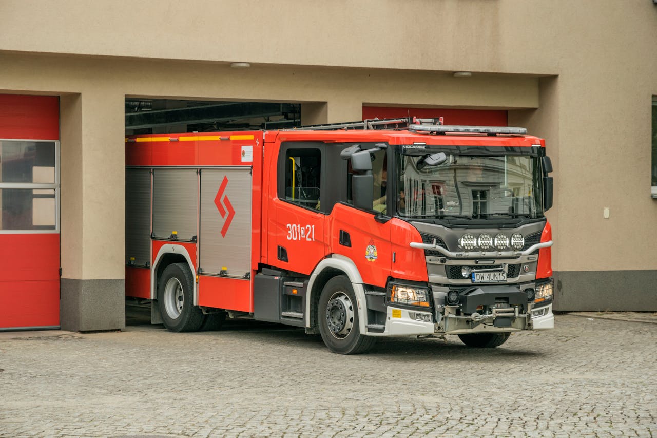 A bright red firetruck leaving a fire station in Wrocław, Poland on a cobblestone street.